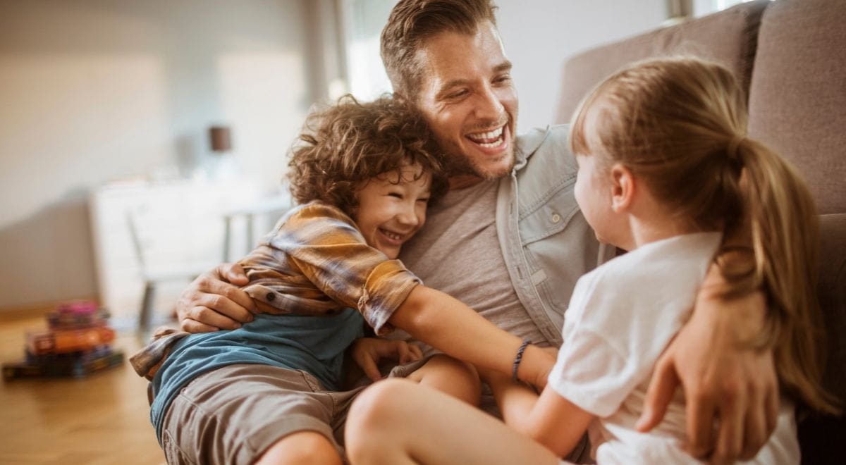 Assegno di inclusione | Fotografia di padre felice che gioca con i due figli in soggiorno