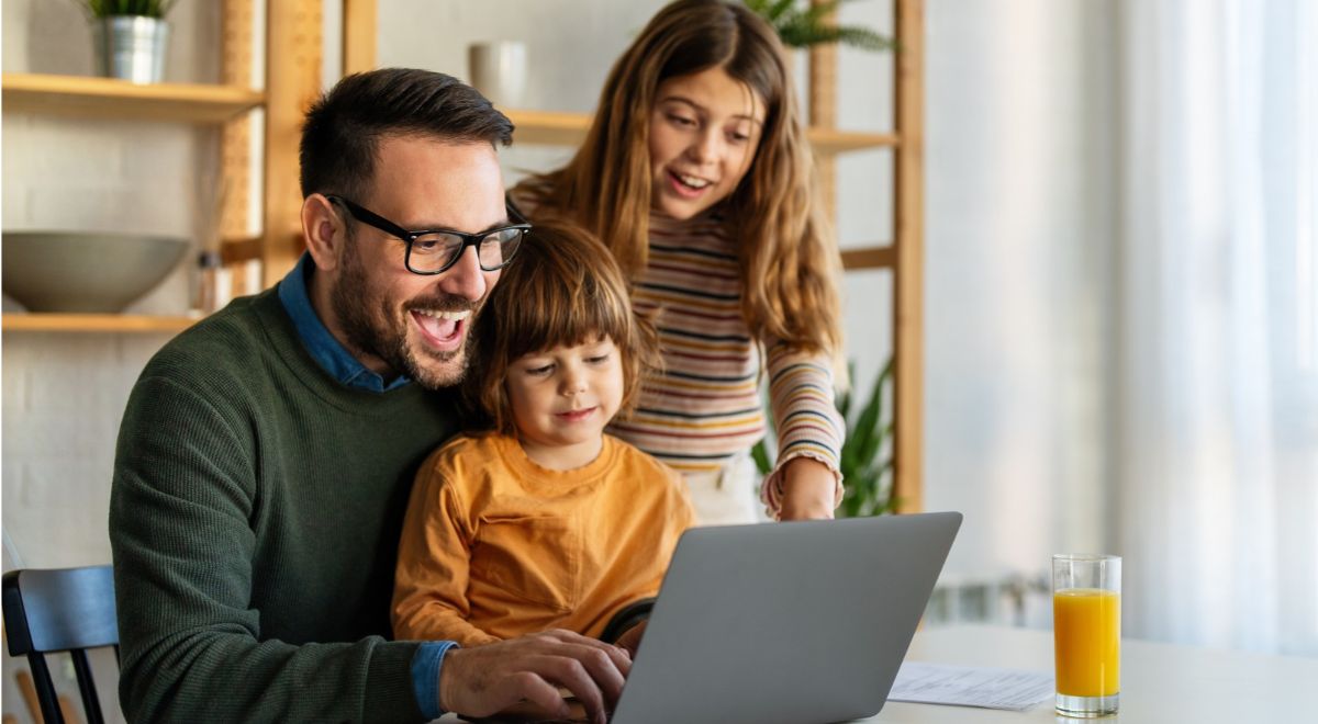 Assegno unico universale | Fotografia di padre sorridente con figli davanti al PC