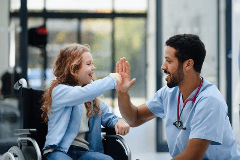 Healthcare | Immagine di un ragazzo che batte il cinque ad una bambina sulla sedia a rotelle