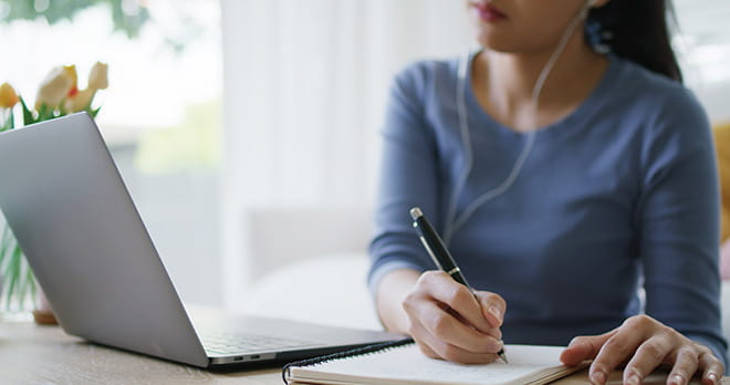 Reskilling e upskilling | Immagine di una donna al computer che prende appunti mentre segue un corso di formazione